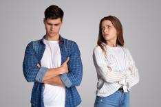 Angry young couple with crossed arms ignoring each other, symbolizing relationship troubles and lack of intimacy, on a gray background