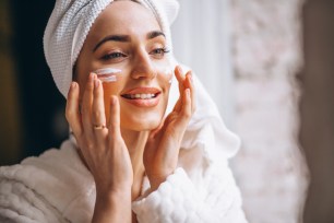 Woman is applying cream on her face.